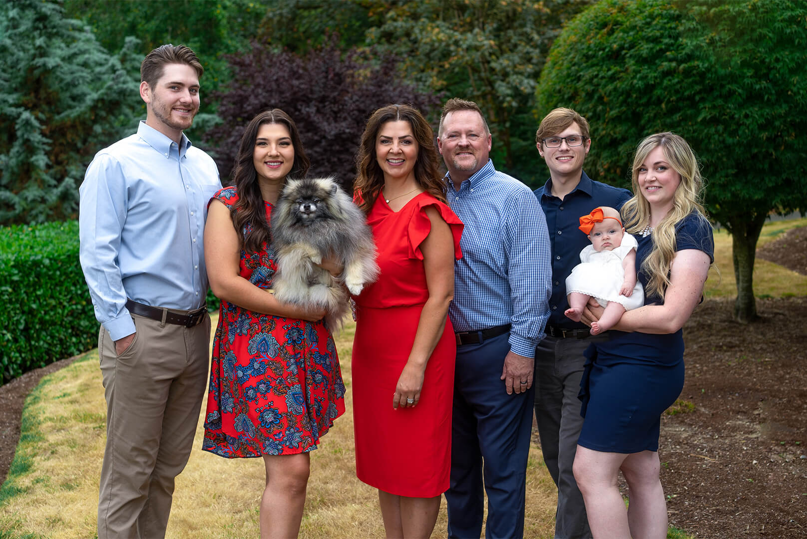Family photo of Kelly Chambers with husband, two children and their significant others, with an infant and a dog outside